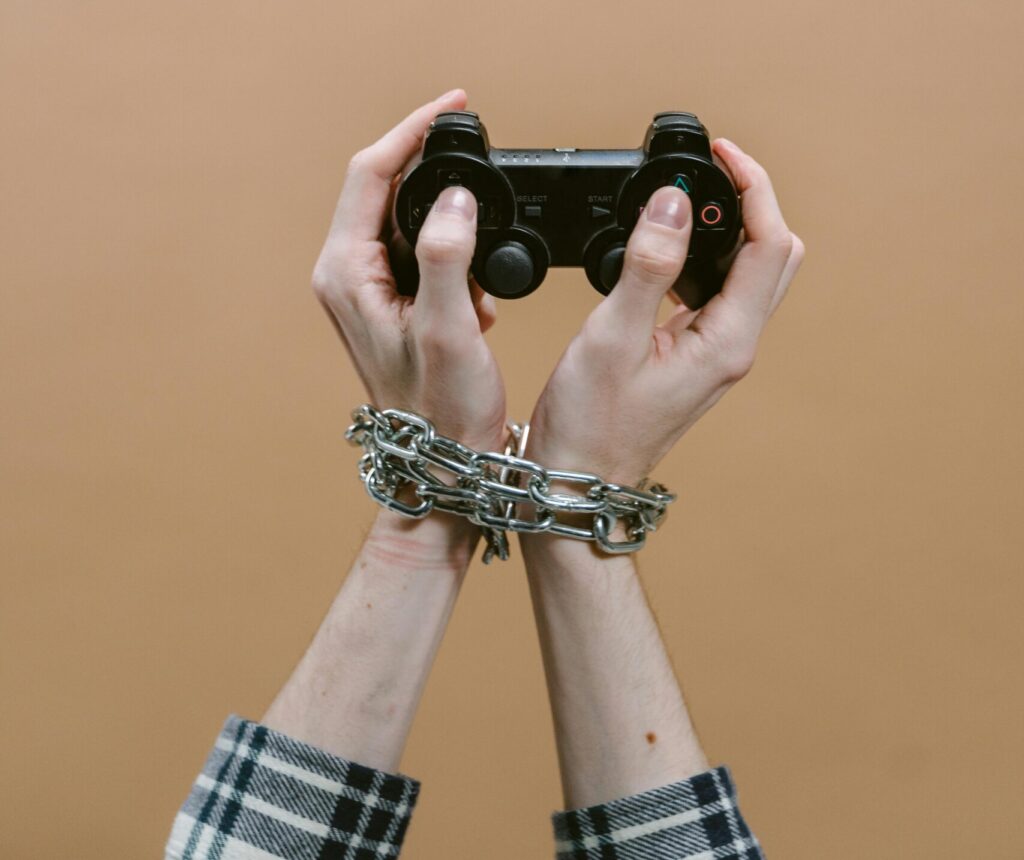 Hands chained playing video game with controller illustrating digital addiction concept.