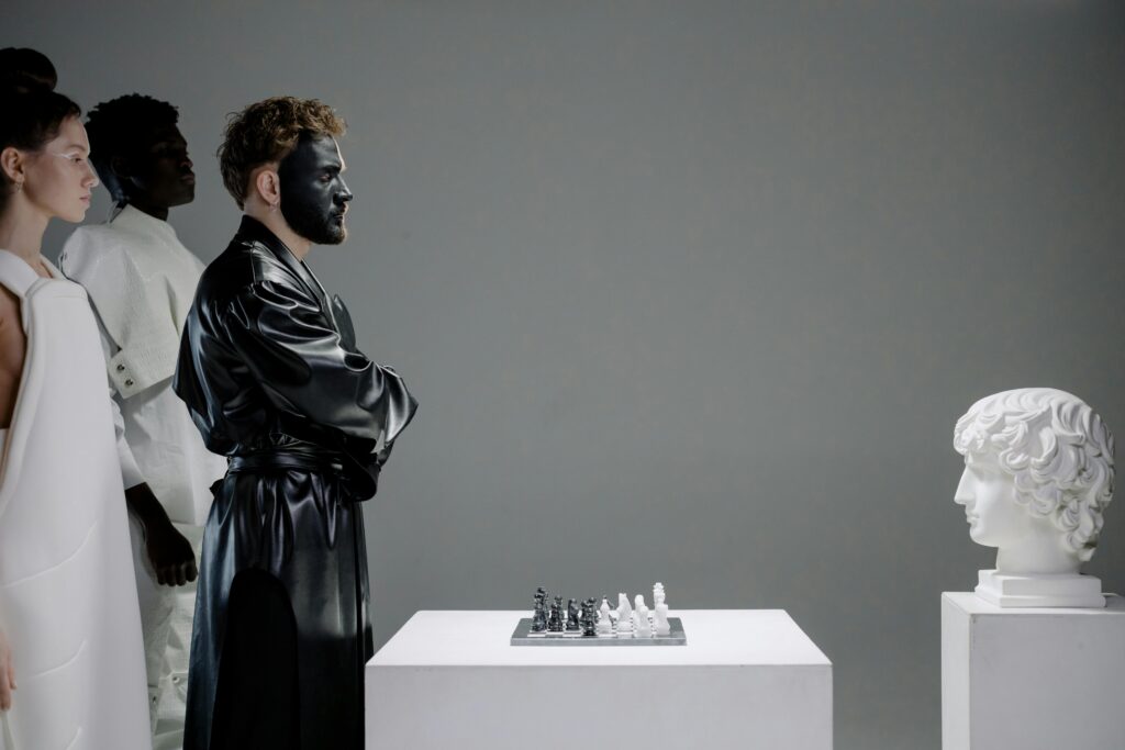 El momento que el ego tomo el control Dramatic studio portrayal of chess game, featuring performers in costume and face paint, alongside a classic sculpture.
