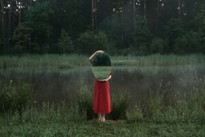 Artistic photo of a woman in nature holding a mirror beside a misty pond.
