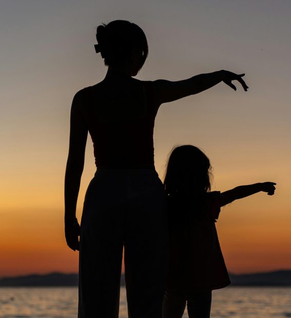 Silhouetted woman and child enjoying a serene sunset by the sea in Supetar.